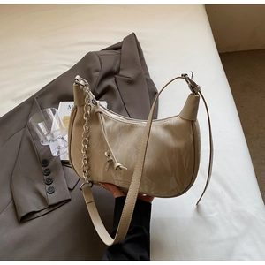 Detail of a beige crescent bag with glossy leather finish and silver chain strap