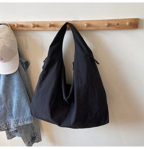 Detail of a large black hobo tote bag in matte fabric hanging on a wooden wall hook