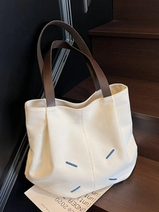 Large cream canvas tote bag with blue stitch accents on dark wooden stairs background