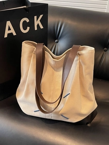 Minimalist beige canvas tote bag with brown leather handles and blue stitching detail