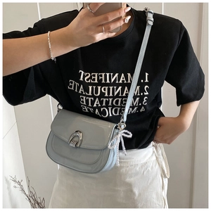 Détail d'un sac selle bleu clair en cuir verni avec boucle argentée et nœud en perles