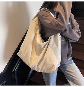 Lifestyle shot showing a large beige canvas hobo bag worn by a model in a minimal setting