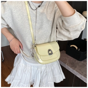 Modèle portant un sac selle en cuir verni jaune avec boucle argentée et breloque perle