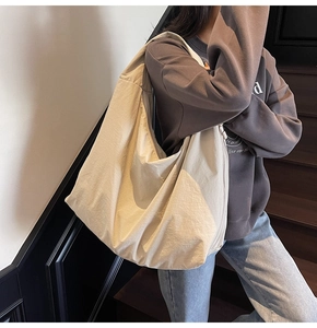 Large beige tote bag with zipper closure and wide shoulder strap shown in a lifestyle setting