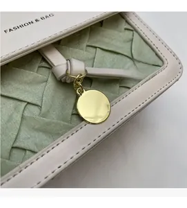 Détail du sac en cuir blanc cassé avec panneau tissé vert et breloque ronde dorée chic