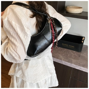 Detail of glossy black half-moon shoulder bag with vintage key woven charm