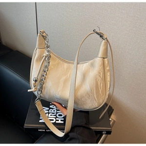 Detail view of beige crescent bag featuring ruched leather texture and silver chain link
