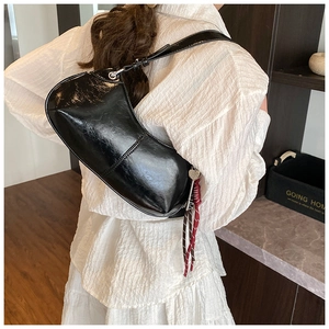 Detail of glossy black patent leather crescent bag with heart charm on a model