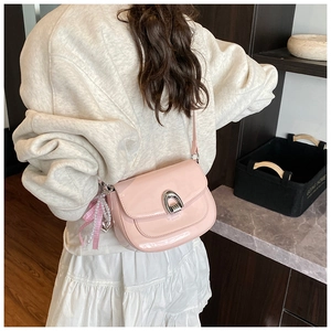 Détail du sac selle en cuir verni rose avec boucle argentée et breloque noeud en perles