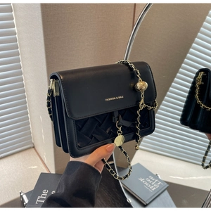 Détail de la texture en similicuir tressé et chaîne dorée sur le sac bandoulière noir