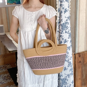 Detail of hand-woven straw tote bag with pink stripe pattern and circular handles
