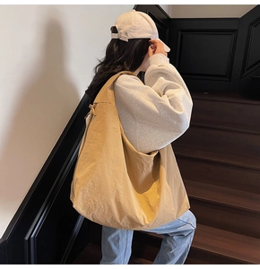 Detail of a large yellow nylon hobo bag shown on a model in a modern urban setting