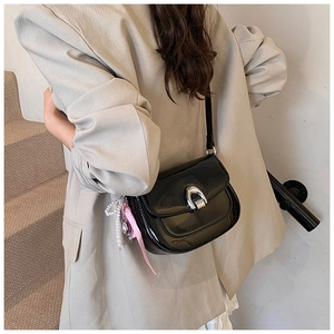 Détail du sac selle en cuir verni noir avec boucle argentée et breloque en perles