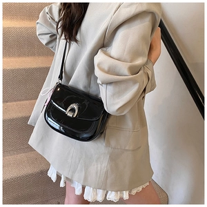 Détail du sac de selle en cuir verni noir avec boucle argentée et breloque en perles
