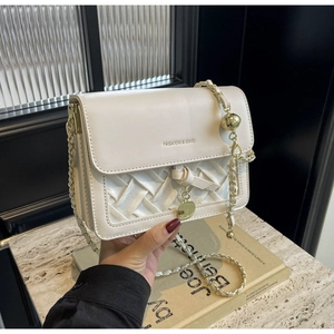 Détail du sac tressé crème avec bandoulière chaîne dorée et ornement boule en métal