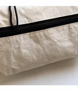 Gros plan détaillé du sac bandoulière beige en nylon avec fermeture éclair noire et tissu