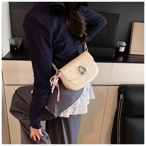 Gros plan du sac de selle en cuir verni crème avec boucle fer à cheval et breloque perle