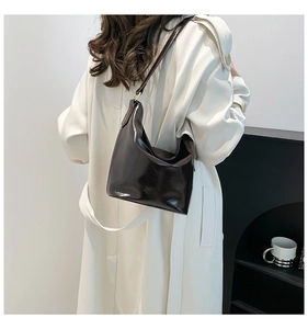 Detail view of dark brown glossy leather underarm bag on a model in white coat