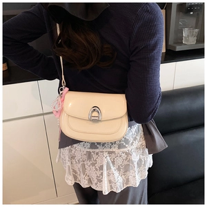 Détail du sac selle en cuir verni blanc cassé avec boucle argentée et nœud en perles