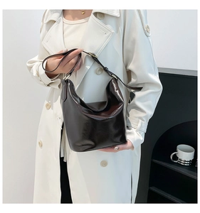 Close-up of a deep coffee glossy leather crescent bag worn with a white coat