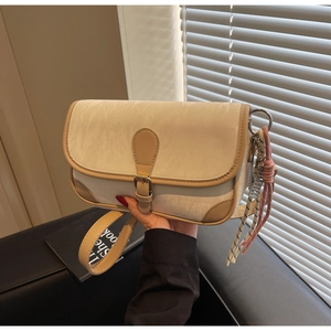 Detail of a vintage cream leather crossbody bag with tan trim and woven rope charm