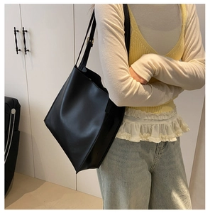 Minimalist black leather tote bag with long shoulder straps shown on casual outfit