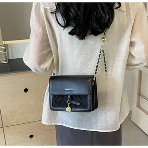 Détail du sac bandoulière noir matelassé avec plaque métal et texture tressée chic