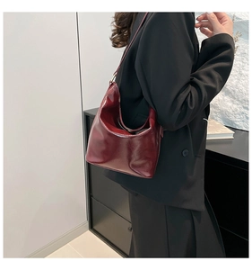 Side view of a burgundy glossy leather crescent shoulder bag worn by a female model