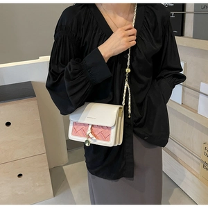 Détail du rabat tissé rose sur un sac à bandoulière en cuir blanc avec pendentif