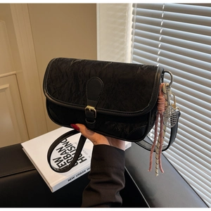 Detail of black pebbled leather crossbody bag with tennis racket charm and gold buckle