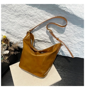 Close-up of caramel glossy leather hobo bag with adjustable strap and gold metal buckle