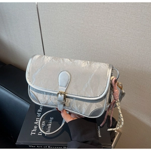 Detail der silbernen PU-Schultertasche mit Knitteroptik und einem modischen Flechtanhänger