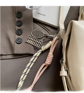 Detail of pink woven rope charm with metal tennis racket and abacus on beige bag