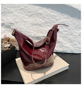Detail of burgundy patent leather bucket bag with glossy texture on stone wall background