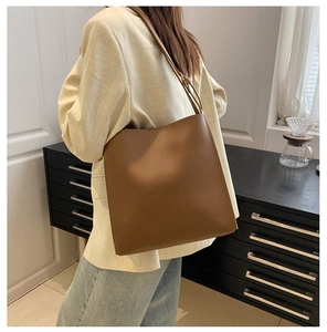 Caramel brown leather tote bag worn as a shoulder bag in a minimalist interior setting