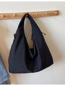 Large black minimalist tote bag with natural texture hanging on a wooden wall hook