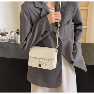 Gros plan du sac bandoulière beige en cuir tressé avec chaîne dorée sur un mannequin