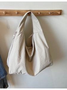 Large beige nylon tote bag with crinkled texture hanging on a wooden rack for casual use