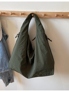 Bolso tote de nailon verde militar con correa ancha colgado en un gancho de madera