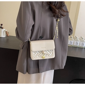 Détail d'un sac crème matelassé avec chaîne dorée et pendentif métallique chic