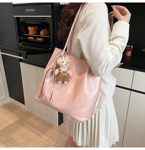 Pink glossy faux leather tote bag with a bear charm shown being worn on the shoulder