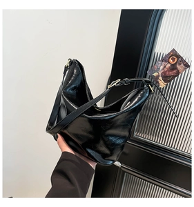 Close-up of black glossy patent leather hobo bag with gold hardware and pleated texture
