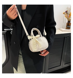 Detail of cream white mini crossbody bag with lace bow accessory on black blazer