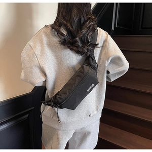 Détail du sac bandoulière noir avec texte blanc et longues fermetures éclair
