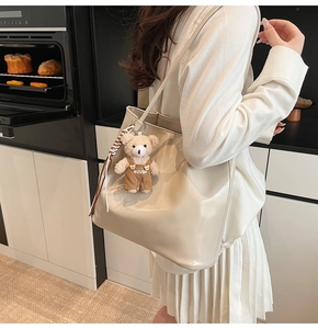 Close-up of a cream tote bag with bear charm worn by a model in a modern kitchen setting