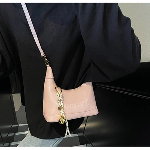 Detail of pink glossy leather crossbody bag with embossed lettering and bell charm