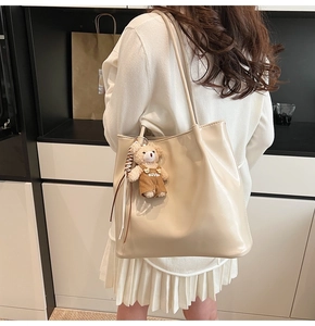 Detail of cream faux leather tote bag with a small bear charm on the shoulder strap
