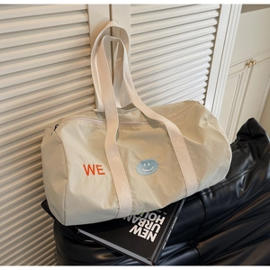 Dettaglio della borsa da viaggio in tela con logo WE arancione e patch smiley blu su beige