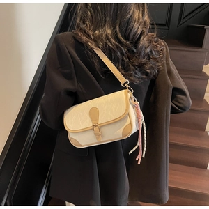 Detail view of cream crossbody bag with tan leather trim on a model in a black blazer