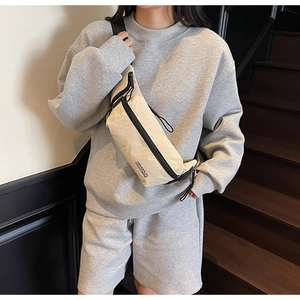 Détail d'un sac bandoulière en nylon beige avec fermeture éclair noire sur look sport